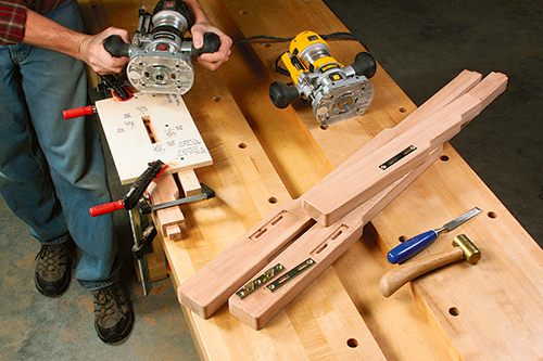 The author clamped a shop-made, slotted mortising jig to the legs, then used two different guide collars and bit sizes to rout the bed rail hardware mortises and prong slots. Chisel the shallow mortises square.