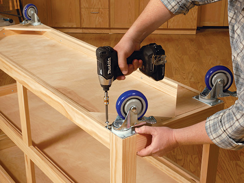 Screwing casters into caster blocks attached to workbench frame